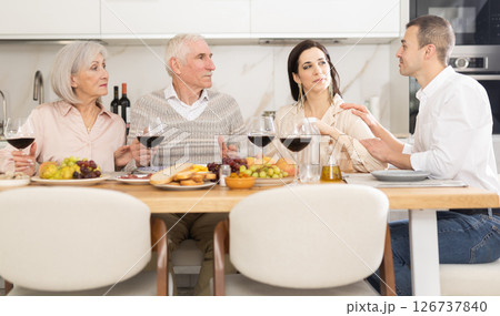 Mature married couple are sitting at table, enjoying food and wine with middle-aged guests. 126737840