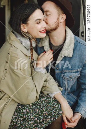 Focus on a woman with red lips and a man with black hat. Romantic couple in fashion clothes hugging. Man wearing jacket and woman coat. Focus on a woman with red lips and a man with black hat. Romantic couple in fashion clothes hugging. Man wearing jacket and woman coat. 126738493
