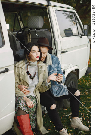 Man and woman in fashion clothes sitting in a bus. Man wearing jacket and a black hat and woman coat and red boots. Photo of romantic couple in a white retro bus. Man and woman in fashion clothes sitting in a bus. Man wearing jacket and a black hat and woman coat and red boots. Photo of romantic couple in a white retro bus. 126738494