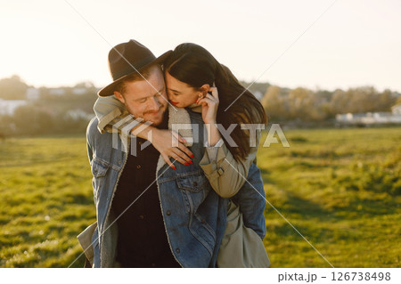 Man and woman in fashion clothes resting on a nature together in sunset. Man wearing jacket and a black hat and woman coat. Photo of romantic couple hugging. 126738498