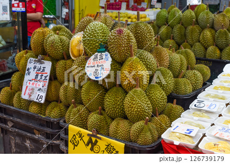 Singapore, Singapore - 4 April 2025: Fresh durians stacked at a local market in Singapore, showcasing Musang King and other varieties with handwritten price signs. Singapore, Singapore - 4 April 2025: Fresh durians stacked at a local market in Singapore, showcasing Musang King and other varieties with handwritten price signs. 126739179