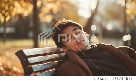 秋の陽だまりに包まれてベンチで眠る青年 126739615
