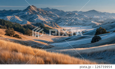 Golden grasslands and frosty hills under clear sky create serene landscape 126739954