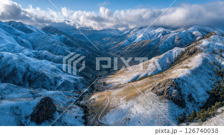 Snow dusted mountains under cloudy sky create serene landscape, with winding path leading through valley 126740038