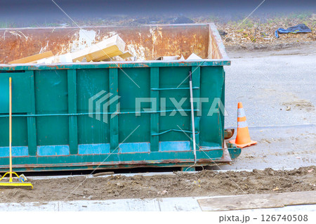 Workers dispose of construction waste in large container located on construction site suburban street Workers dispose of construction waste in large container located on construction site suburban street 126740508