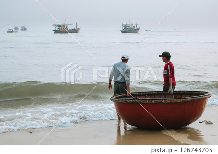 Vietnamese male fishermen with a traditional Vietnamese round basket boat on the beach by the sea in a village in Vietnam 126743705