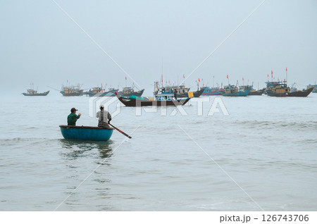 Vietnamese fishing ships and traditional round basket boats with fishermen at sea in morning in a fishing village in Vietnam Vietnamese fishing ships and traditional round basket boats with fishermen at sea in morning in a fishing village in Vietnam 126743706