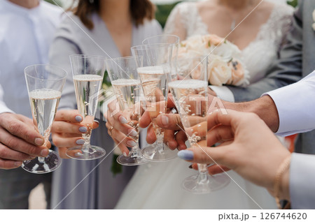A joyous wedding toast with champagne glasses clinking in celebration among elegantly dressed guests, featuring a bride and groom as the focal point of the event 126744620