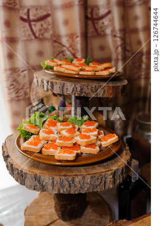Elegant canapes with red caviar on wooden tiered serving stands in a rustic setting, featuring a natural wood backdrop and refined presentation for a formal event 126744644