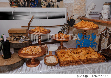A lavish snack buffet is displayed on a table with wooden stands holding various chips and savory bites, decorated with nautical elements like a blue crab and fishing tools 126744647