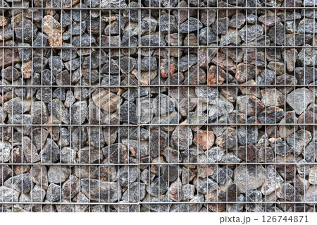 Close-up view of a metal wire fence frame filled with rocks. Gabion 126744871