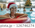 Beautiful happy woman in Santa Claus hat with inflatable ring relaxing in blue swimming pool 126746274