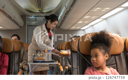 Flight attendant in beige uniform with red scarf serves meal to passenger on airplane. Flight attendant in beige uniform with red scarf serves meal to passenger on airplane. 126747739