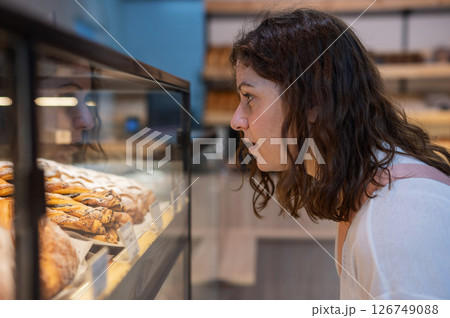 Caucasian woman looks greedily at baked goods in a bakery.  126749088