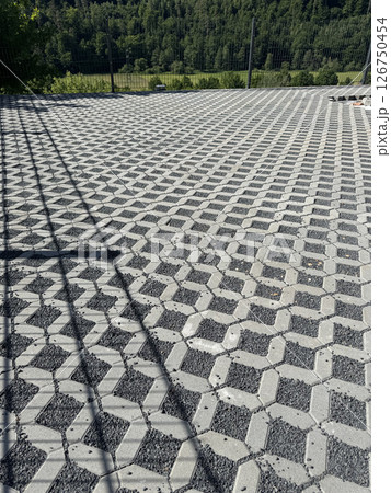 A wide view of geometric concrete pavers arranged in a seamless pattern. These pavers are set outdoors, bordered by a lush green forest, creating an elegant and durable surface. 126750454