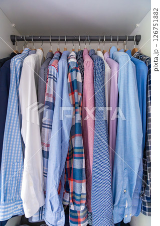 Neatly arranged men shirts hanging on wooden hangers in wardrobe. Minimalist clothing organization and classic male fashion concept Neatly arranged men shirts hanging on wooden hangers in wardrobe. Minimalist clothing organization and classic male fashion concept 126751882