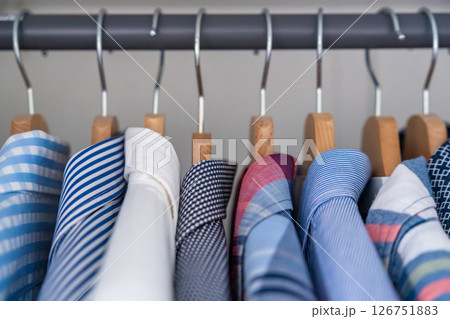 Neatly arranged men shirts hanging on wooden hangers in wardrobe. Minimalist clothing organization and classic male fashion concept 126751883