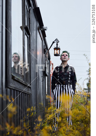 A Stylish Individual Posing Confidently Near a Vintage Cabin in a Beautiful Setting A Stylish Individual Posing Confidently Near a Vintage Cabin in a Beautiful Setting 126753108
