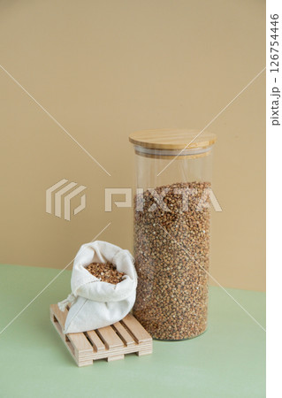 Refillable glass jar with raw buckwheat porridge and cotton bag. Copy space Refill product format eco-friendly living. Filling reusable container Whole spelt grain species. High protein fiber-rich 126754446