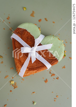 Gift present idea for love Valentine's Day holiday celebration Heart shaped pistachio croissant on green background with copy space. Puff pastry trendy sweet dessert bakery. Creamy dough experiment  126754475