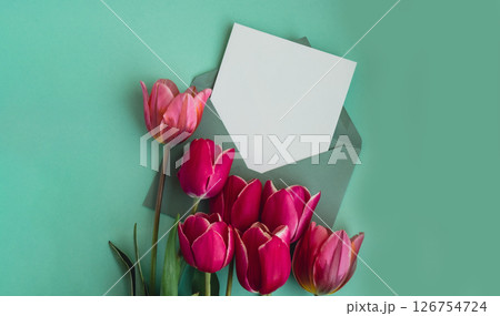 Empty white envelope copy space for your text or design with beautiful pink tulip bouquet on green background. Template mock up for holiday spring greeting card. Top view Flat lay blank paper Feminine 126754724
