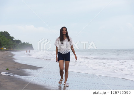 young woman walking alone on the beach near the sea waves 126755590