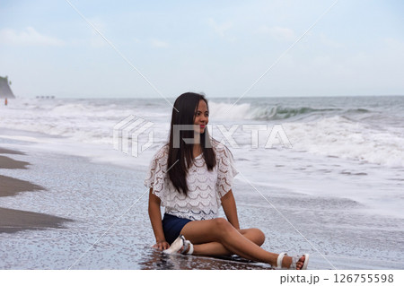 Happy woman sitting on the beach with waves in the background 126755598