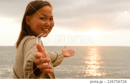 A Radiantly Joyful Woman Embracing the Beautiful Golden Sunset by the Calm Ocean Waves at Dusk A Radiantly Joyful Woman Embracing the Beautiful Golden Sunset by the Calm Ocean Waves at Dusk 126756726