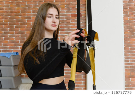 Woman adjusting suspension straps before workout in gym. 126757779