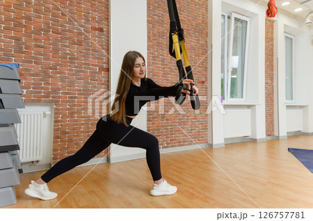 Young woman in sports clothing training with trx fitness straps in the gym. 126757781