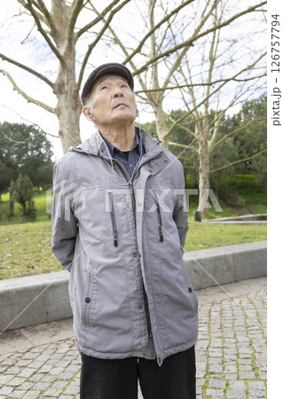 Elderly asian man listening to music in park looking up Elderly asian man listening to music in park looking up 126757794