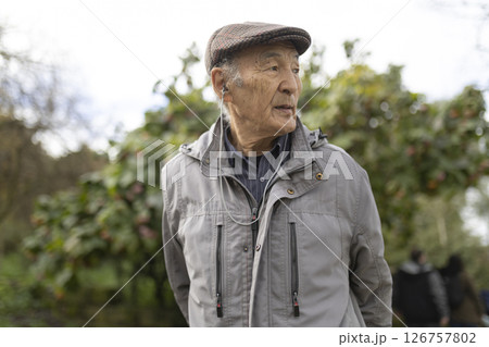 Elderly asian man enjoying music in park wearing earbuds and flat cap Elderly asian man enjoying music in park wearing earbuds and flat cap 126757802