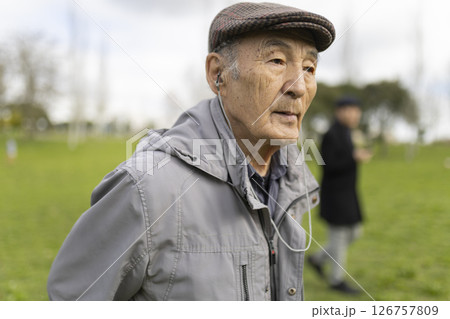 Senior man enjoying music during a relaxing walk in a green park 126757809