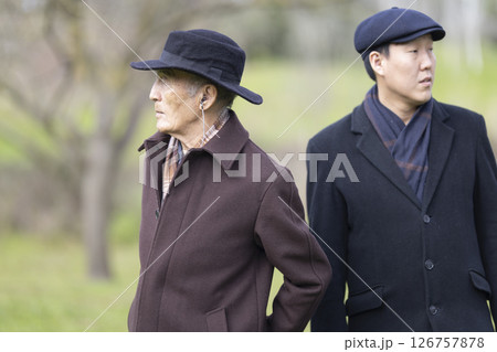 Two senior asian men wearing hats and coats standing in park Two senior asian men wearing hats and coats standing in park 126757878