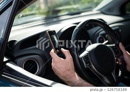 Man driving a car while using a smartphone, representing the danger of distracted driving and lack of attention on the road. 126758189