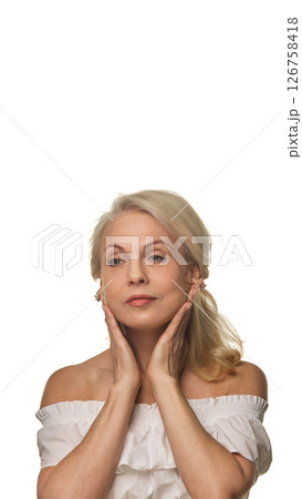 Graceful older woman presses hands to jawline, massaging face against white background, showing confident aging and daily facial care Graceful older woman presses hands to jawline, massaging face against white background, showing confident aging and daily facial care 126758418