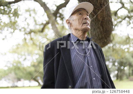 Elderly asian man enjoying music in park: wearing a baseball cap and earphones 126758448