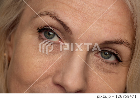Extremely close-up of mature woman's eyes with soft makeup showing natural wrinkles and smooth skin against black background. Extremely close-up of mature woman's eyes with soft makeup showing natural wrinkles and smooth skin against black background. 126758471