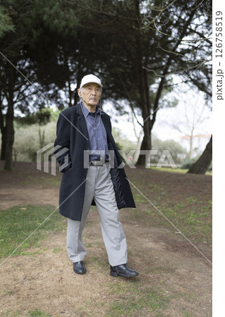 Elderly man wearing a cap and coat walking in a park 126758519