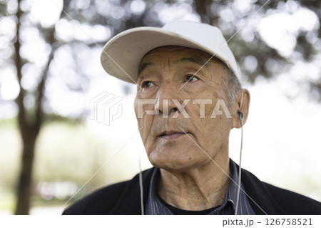 Senior asian man listening music with earphones outdoors in a park 126758521