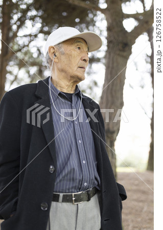 Senior man listening music with earphones in park Senior man listening music with earphones in park 126758522
