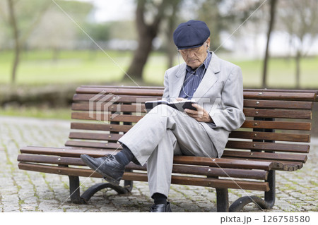 Elderly writer taking notes in a notebook while sitting on a bench in the park 126758580