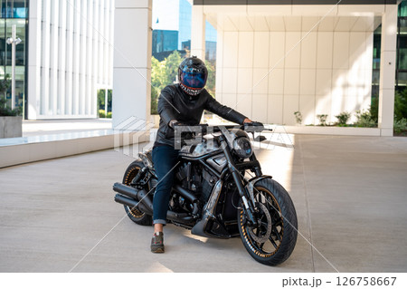 Handsome biker with helmet sitting on his moto against urban backdrop. High quality photo 126758667