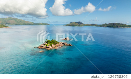 A small, rocky island covered in greenery sits in the middle of expansive turquoise waters. St Pierre, Curieuse Islands. Seychelles. 126758805