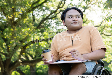 Disabled artist in wheelchair enjoying coffee while sketching in a lush green park Disabled artist in wheelchair enjoying coffee while sketching in a lush green park 126759852