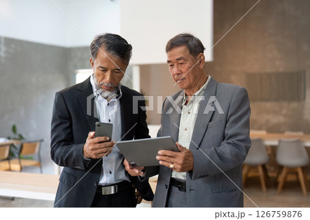 Elderly man checking smartphone while reviewing tablet 126759876
