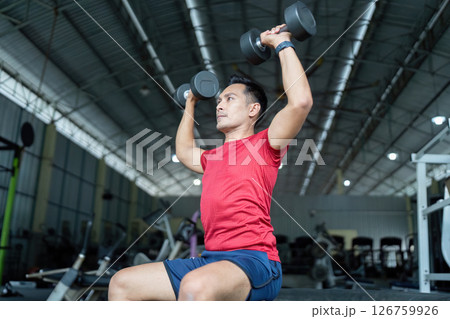 Wellness and Strength Training. Man performing an overhead dumbbell press in the gym. Wellness and Strength Training. Man performing an overhead dumbbell press in the gym. 126759926