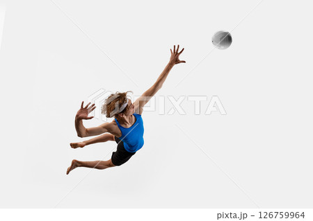 High angle view of jumping athlete extends one hand high above in dynamic motion as volleyball approaches against white studio background. 126759964
