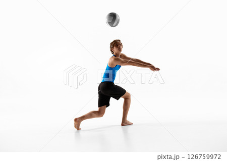 Dynamic photo of young male volleyball athlete, in blue shirt, focused on ball to make powerful hit and score goal against white background 126759972