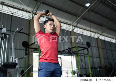 Wellness and Strength. Individual lifting dumbbells overhead in a fitness center. 126760001
